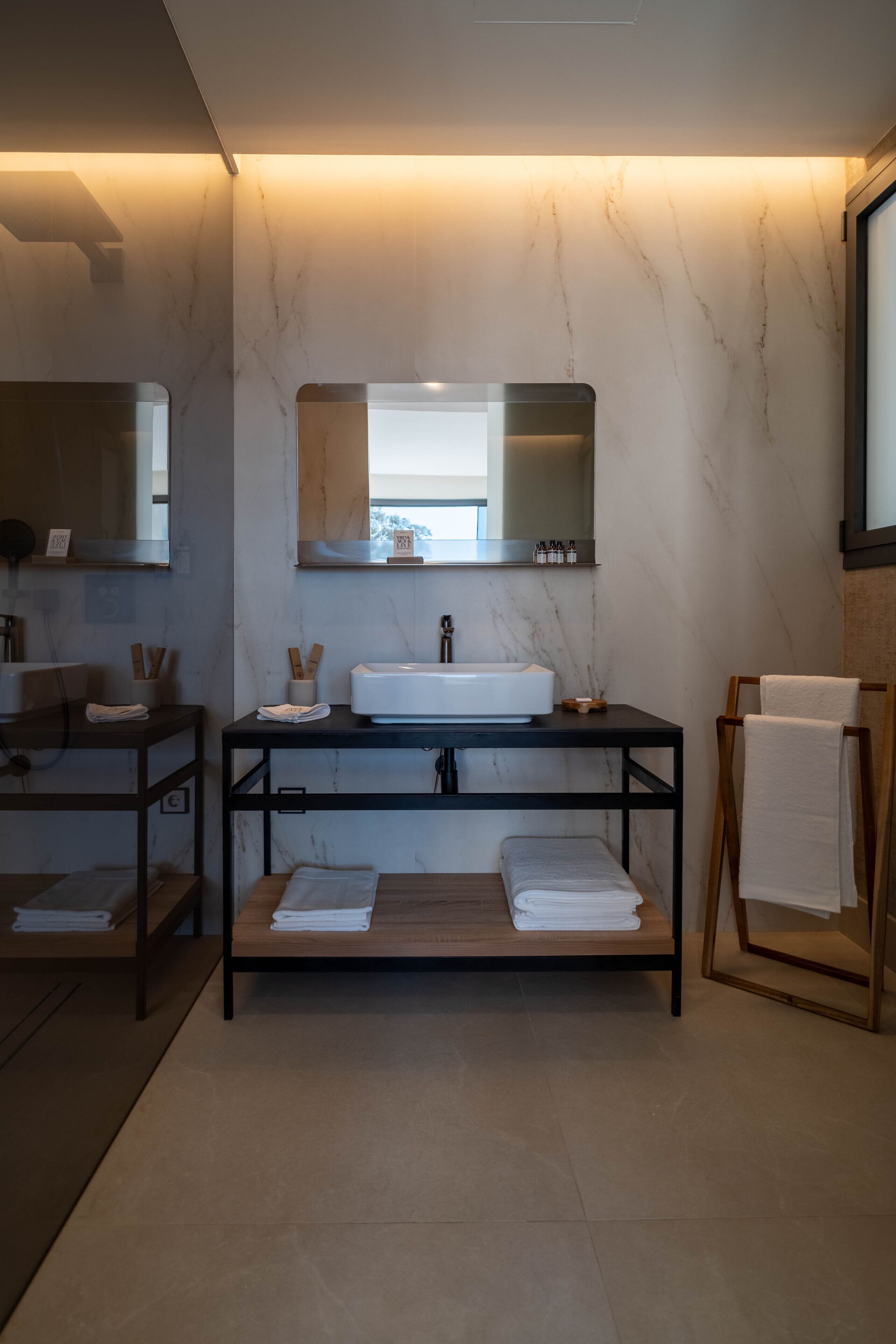 A modern bathroom with a marble wall, a central sink, and a wooden vanity.