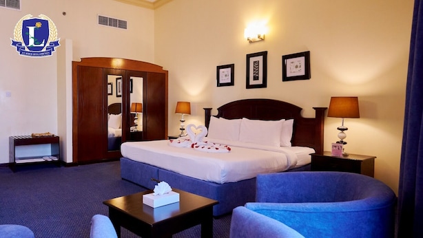 Habitación de hotel con una cama grande, dos mesitas de noche con lámparas, un armario, una pequeña mesa con caja de pañuelos y dos sillones.
