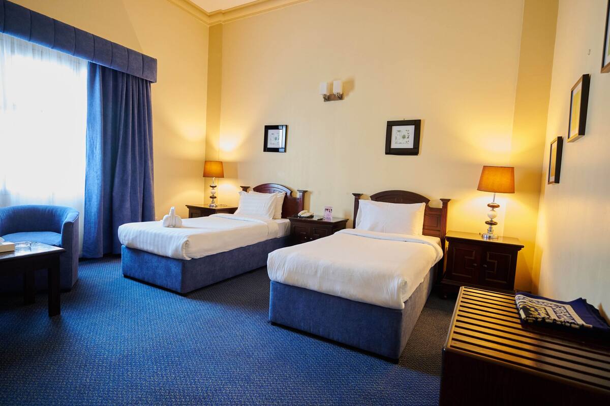 Hotellihuone, jossa on kaksi sänkyä, työpöytä, tuoli ja pieni pöytä.