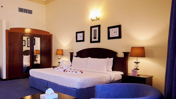 A hotel room with a large bed, two bedside tables with lamps, a wardrobe, a small table with a tissue box, and two armchairs. - La Rosa Hotel Juffair (Manama)