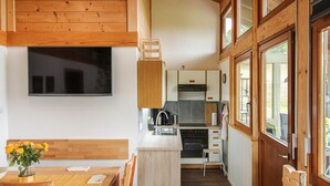 A compact kitchen with a built-in oven, a sink, and a stove. There is a dining area with a wooden table and chairs, and a TV mounted on the wall.