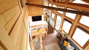 A wooden cabin interior with a dining area, kitchen, and a sofa with a view.