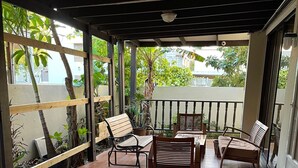 A covered patio area with tiled flooring, wooden furniture, and a view of greenery outside. - Punta Salinas Oasis (Toa Baja)
