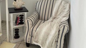 A modern living room with a striped sofa, a small table with decorative items, and a staircase. - Punta Salinas Oasis (Toa Baja)
