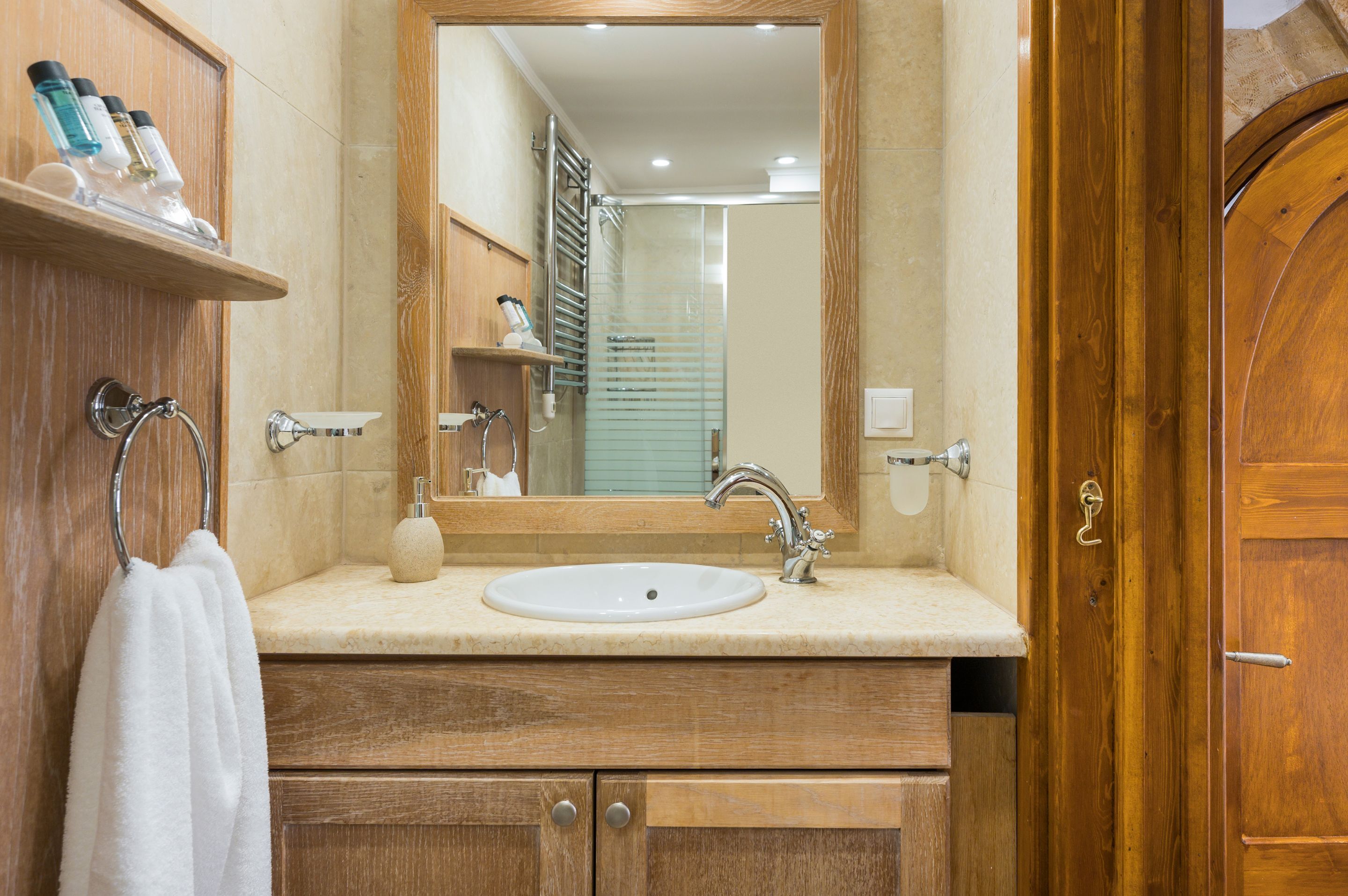Ein Badezimmer mit einem Holzkosmetikschrank, einem Waschbecken, einem Spiegel und einem Handtuchhalter.