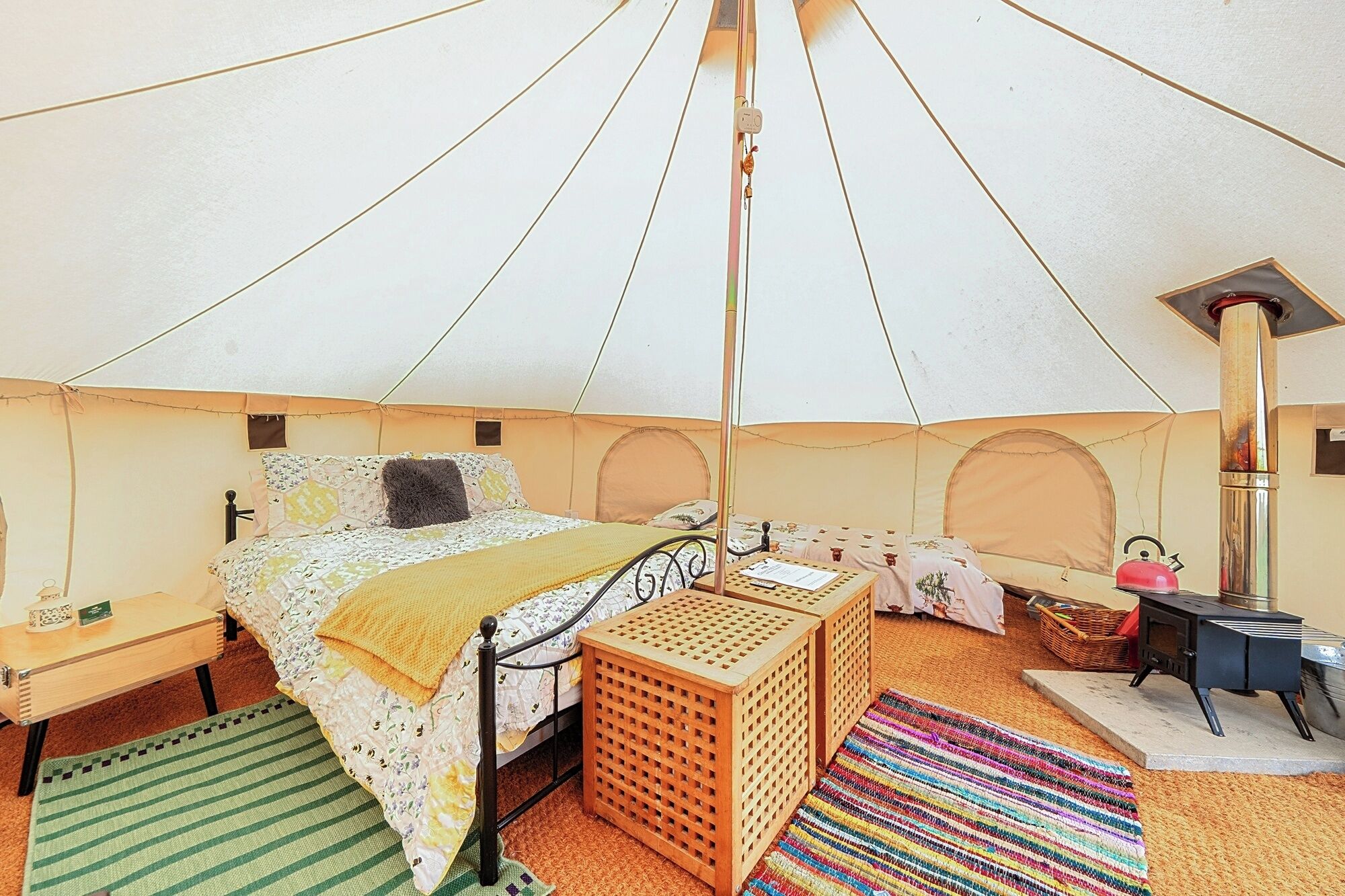 Uma tenda com uma cama, uma mesinha, uma chaleira e uma lareira.