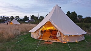 A large, white, pyramid-shaped tent with a cozy interior, set in a grassy field with other similar tents in the background. - Rowan 6m xl Bell Tent (Saltburn-by-the-Sea)