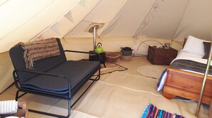 A cozy, compact room with a sofa, a small table with a kettle, a bed, and a fan. - Rowan 6m xl Bell Tent (Saltburn-by-the-Sea)