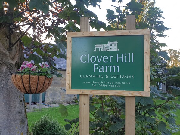 Señal de Clover Hill Farm que anuncia glamping y cabañas, con un número de contacto y sitio web.