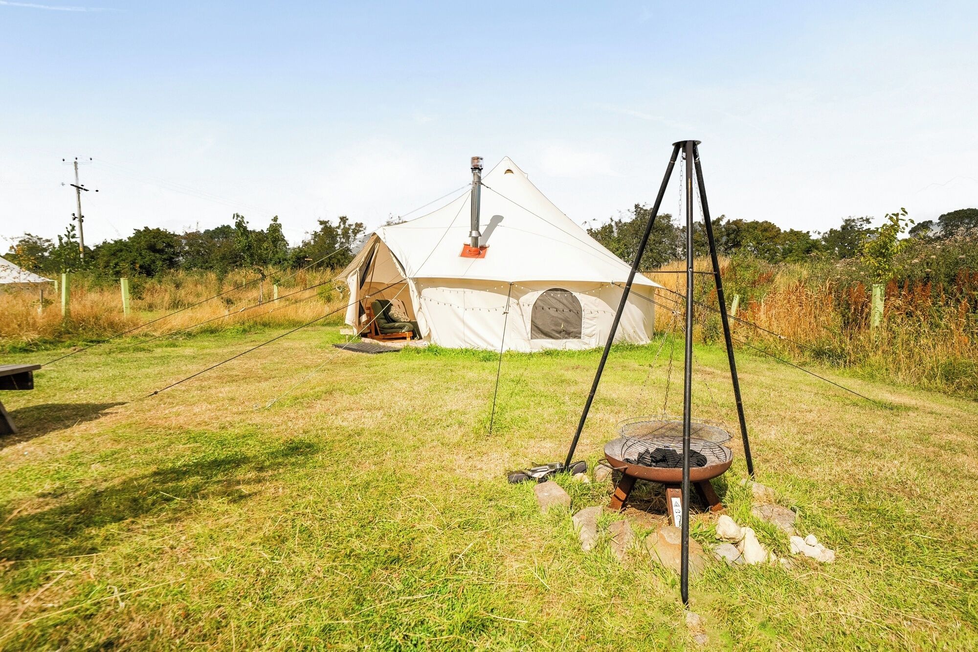 A tent with a chimney, a grill, and a chair outside.