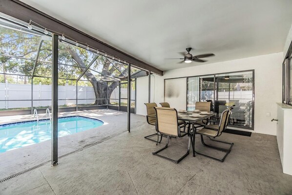 A covered patio with a pool, a dining table with chairs, and a ceiling fan.