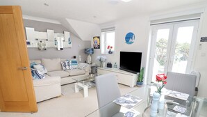 Ett modernt vardagsrum med ett matbord i glas, en soffa, en tv och ett stort fönster.