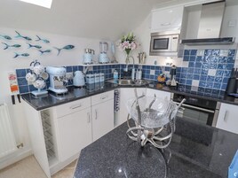 Una cocina moderna con armarios blancos, encimera de granito negro, microondas, hervidor y licuadora. Se aprecia un cuadro de peces decorativos y un jarrón con flores sobre la encimera.
