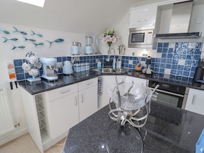 A modern kitchen with white cabinets, a black granite countertop, a microwave, a kettle, and a blender. There is a decorative fish wall art and a vase with flowers on the counter.