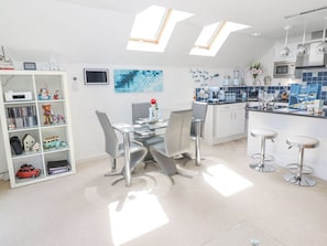 A modern kitchen with skylights, a dining area with a glass table, and a bar area with stools.