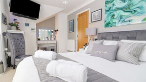Ett hotellrum med en säng, en sminkbord med spegel, en tv och konstverk på väggarna.
