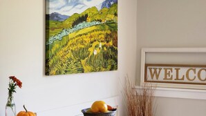 Una mesa de comedor con platos, cubiertos, un cuenco de fruta, un jarrón con flores y un cuadro en la pared.