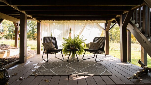 Un patio techado con dos sillas, una mesa y una planta en maceta.