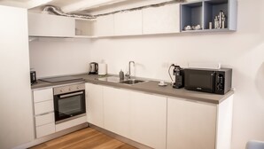Eine kleine Küche mit weißen Schränken, Backofen, Mikrowelle und Kaffeemaschine.
