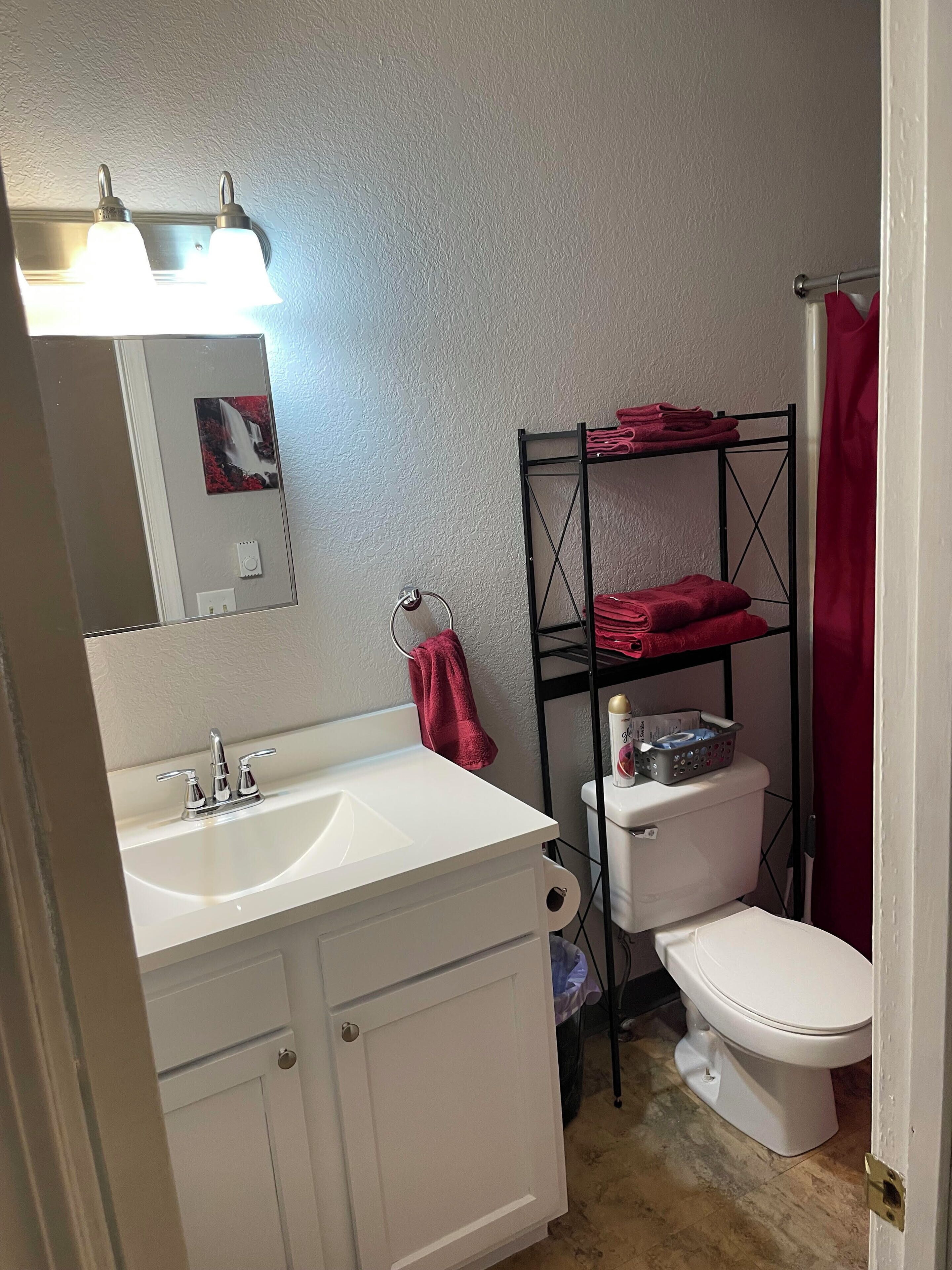 A bathroom with a white sink, a mirror, a toilet, and a metal shelf with towels.