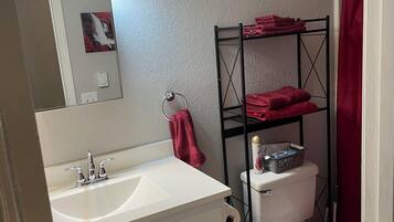 A bathroom with a white sink, a mirror, a toilet, and a metal shelf with towels.