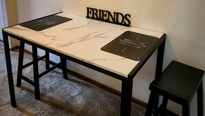 Spisebord med marmorplade, sorte ben og et indrammet kunstværk over. Under kunstværket står ordet "FRIENDS".
