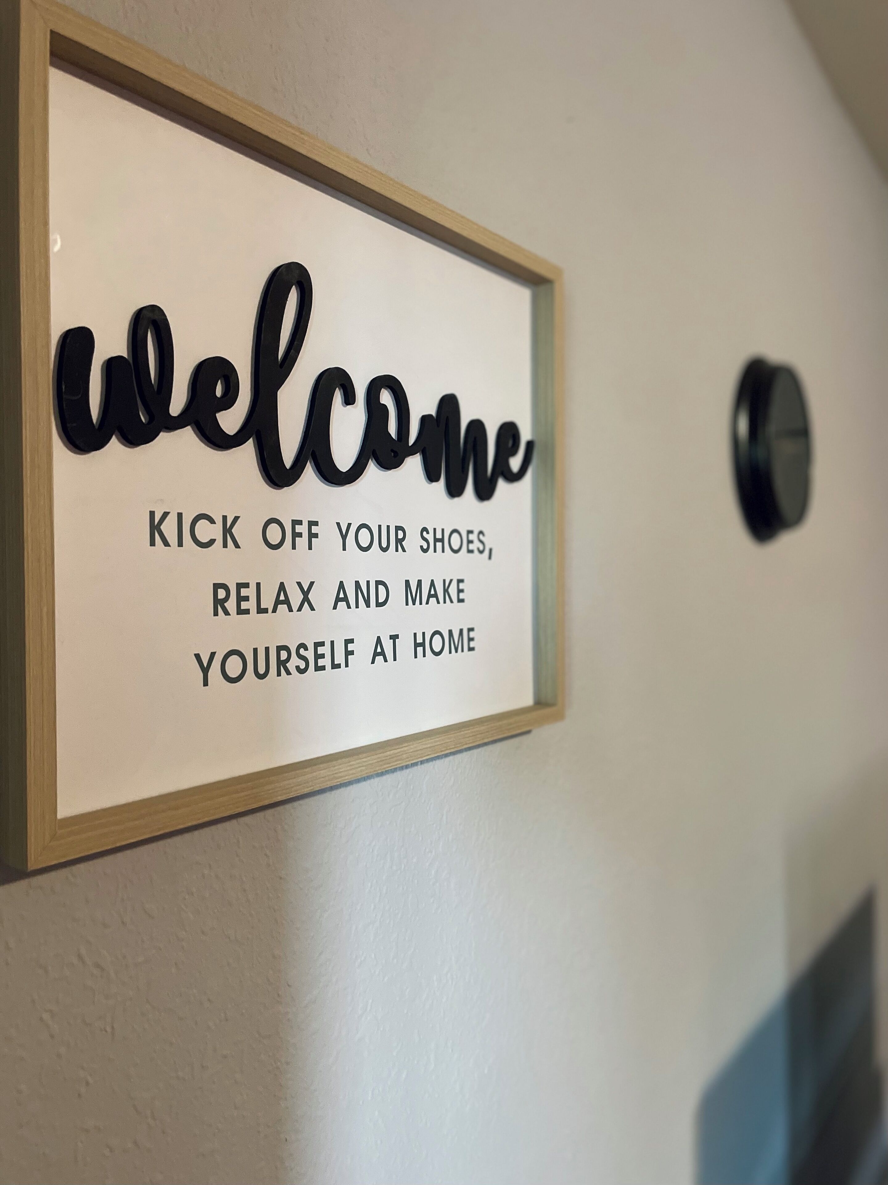 Une pancarte d’accueil avec l’inscription « ENLEVEZ VOS CHAUSSURES, DÉTENDEZ-VOUS ET INSTALLEZ-VOUS COMME CHEZ VOUS », présentée dans un cadre.