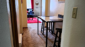 Et tæppe beklædt gangareal, der fører til et spiseområde med et bord og stole.