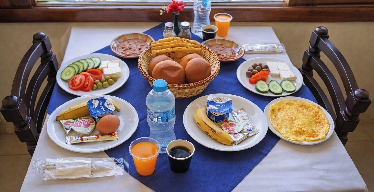 Una mesa de desayuno con diferentes alimentos, como pan, huevos y frutas, además de bebidas y salsas.