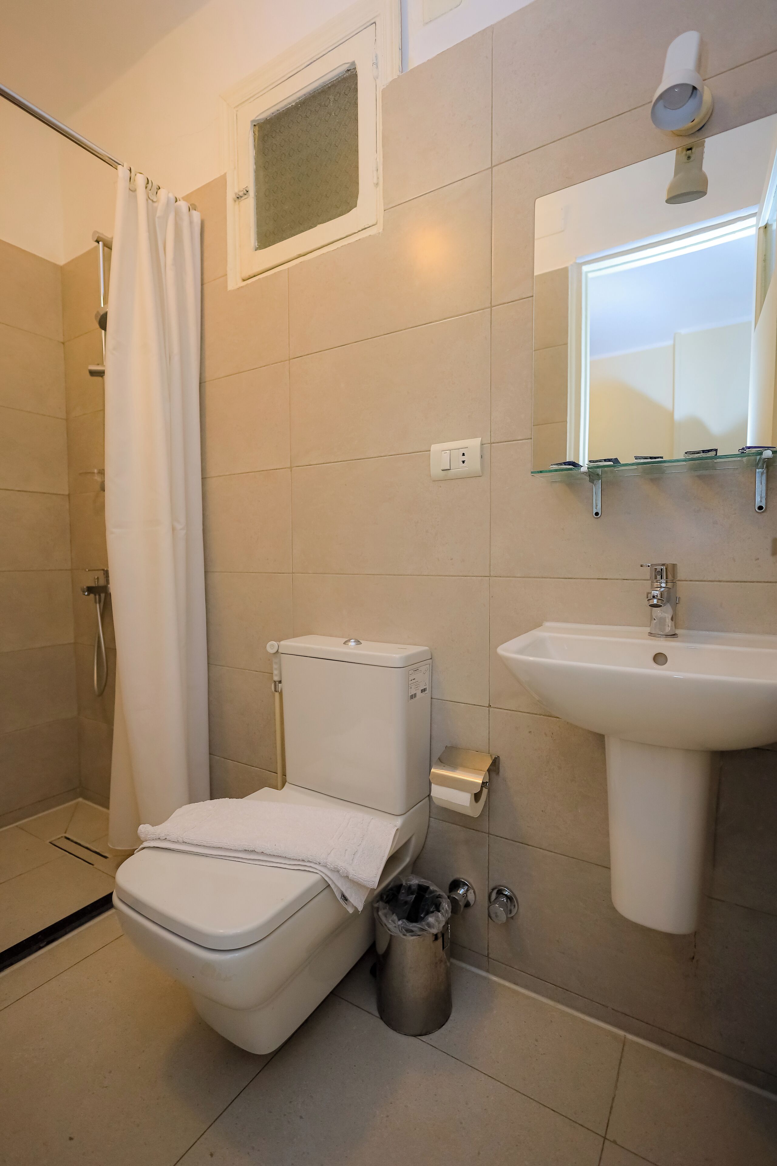 Ein Badezimmer mit Toilette, Dusche, Waschbecken und einem kleinen Fenster über dem Spiegel.