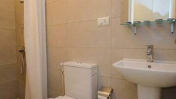 Ein Badezimmer mit Toilette, Dusche, Waschbecken und einem kleinen Fenster über dem Spiegel.