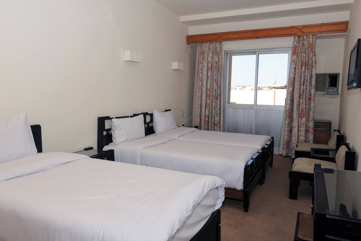 A hotel room with two beds, a desk, a chair, a television, and a window with curtains.