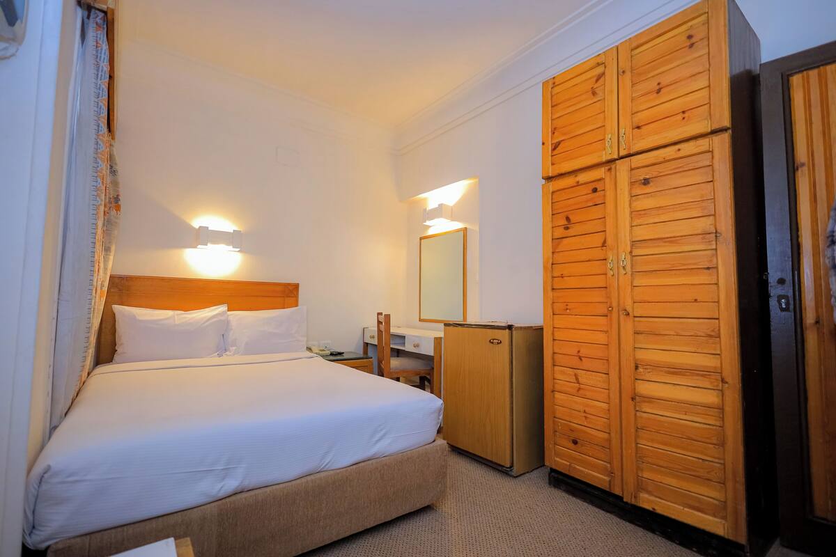 A hotel room with a bed, a desk, a wardrobe, and a mirror.