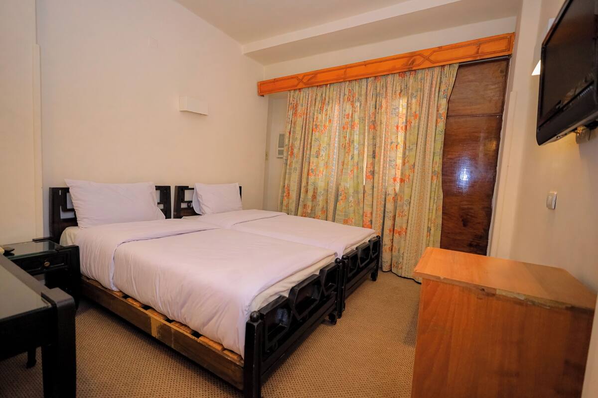 A bedroom with a wooden bed frame, a nightstand, a wooden dresser, and a television mounted on the wall.