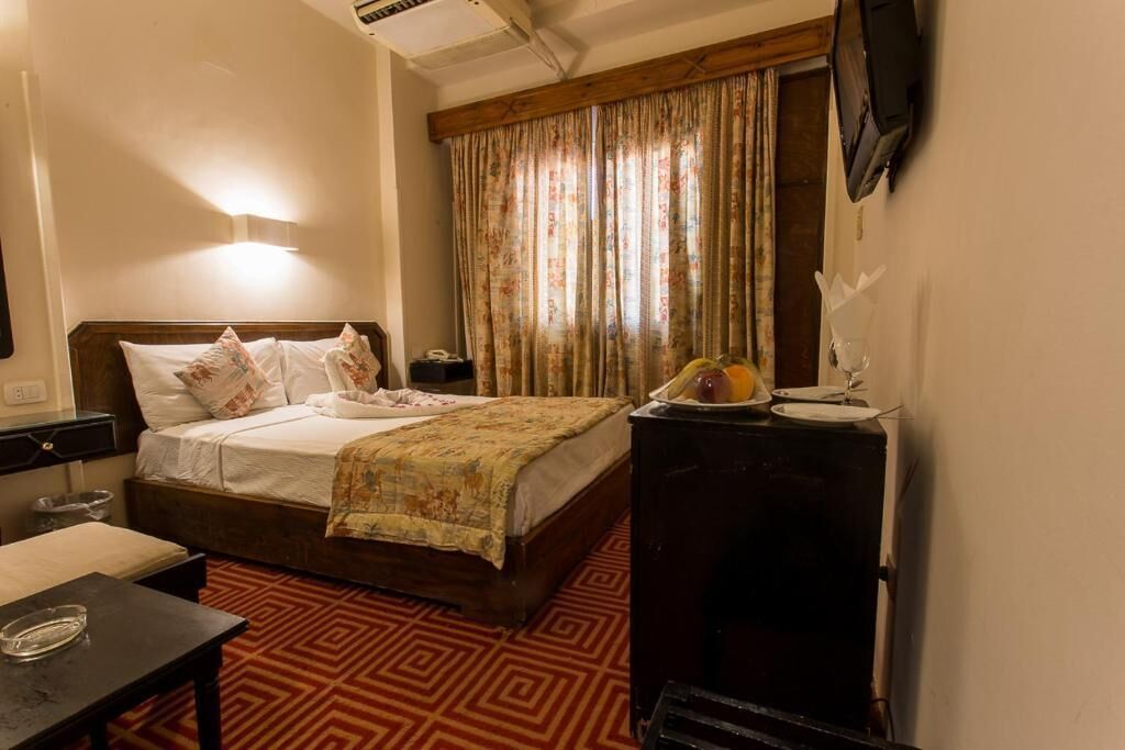 A hotel room with a bed, bedside table, and a television on a stand.