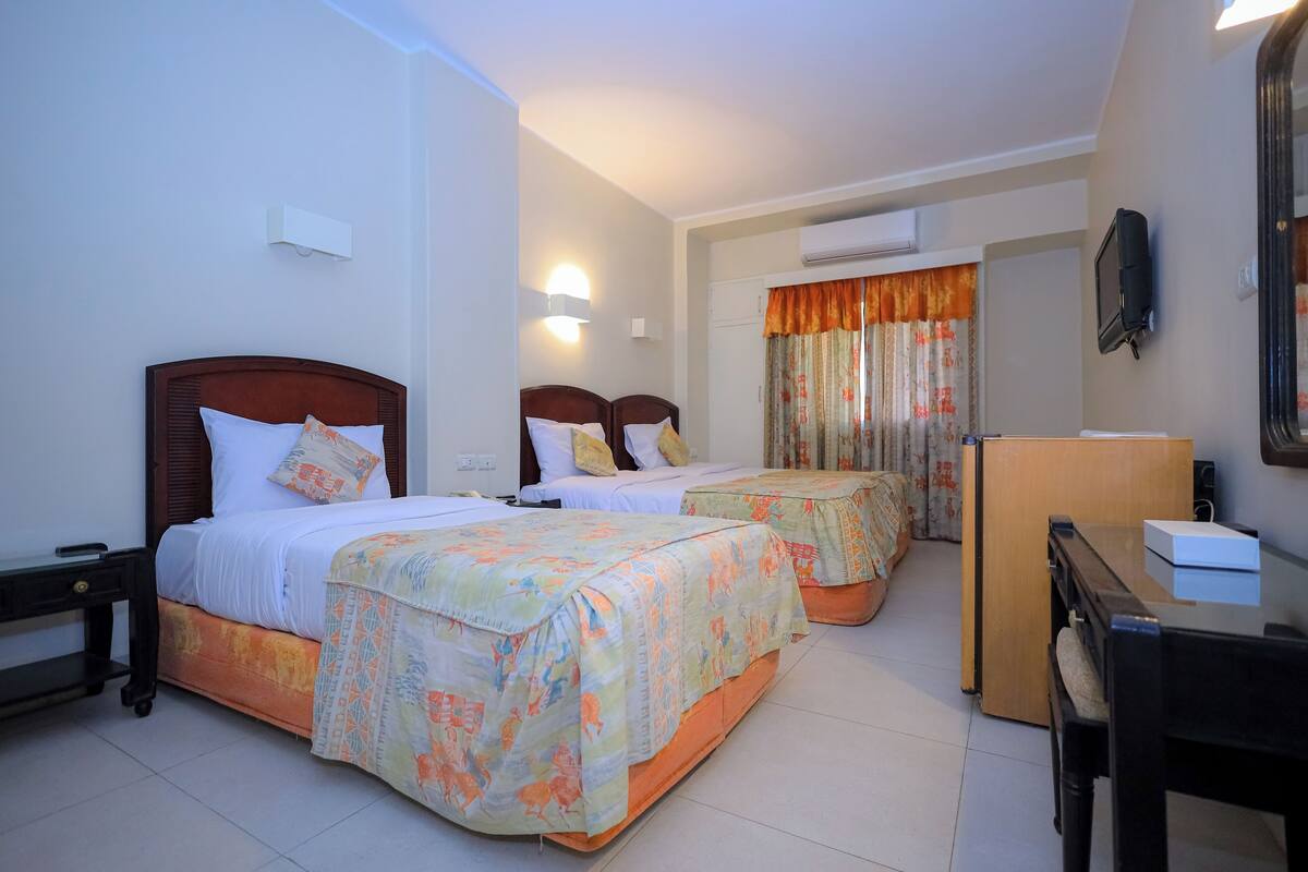 A hotel room with two beds, a desk, a chair, a mirror, and a television.
