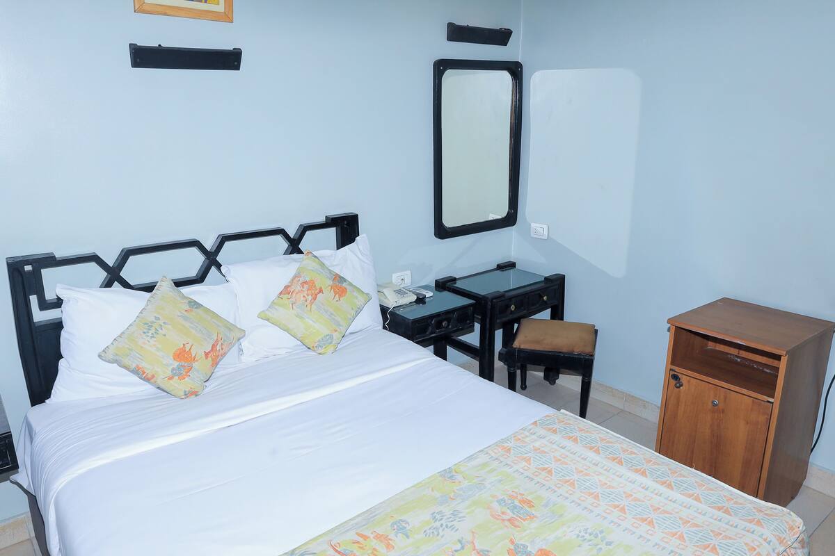 A neatly arranged hotel room with a bed, a desk, a chair, and a small wooden cabinet.