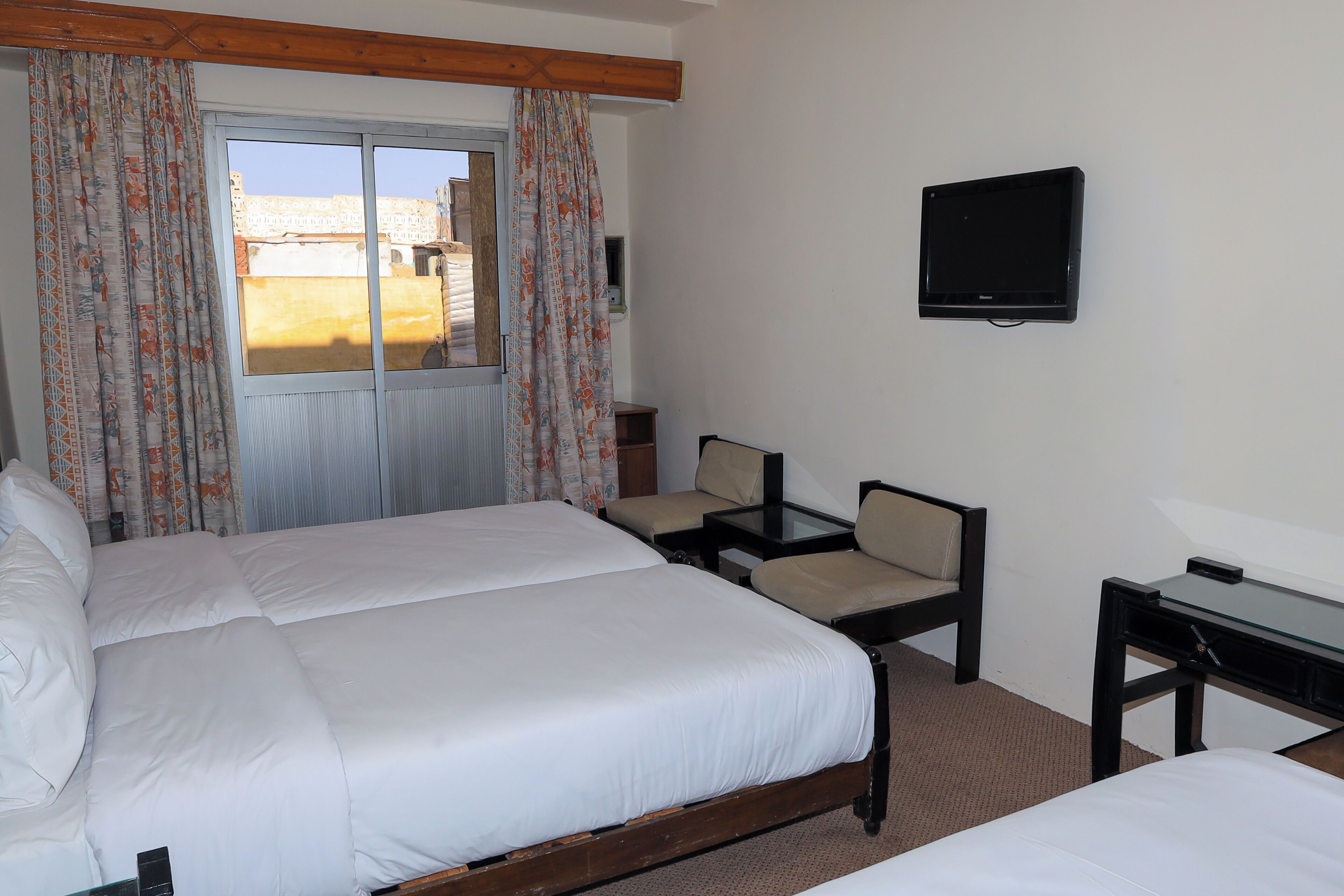 Ein Hotelzimmer mit einem großen Bett, einem Schreibtisch, einem Stuhl, einem Fernseher und einem Fenster mit Vorhängen.