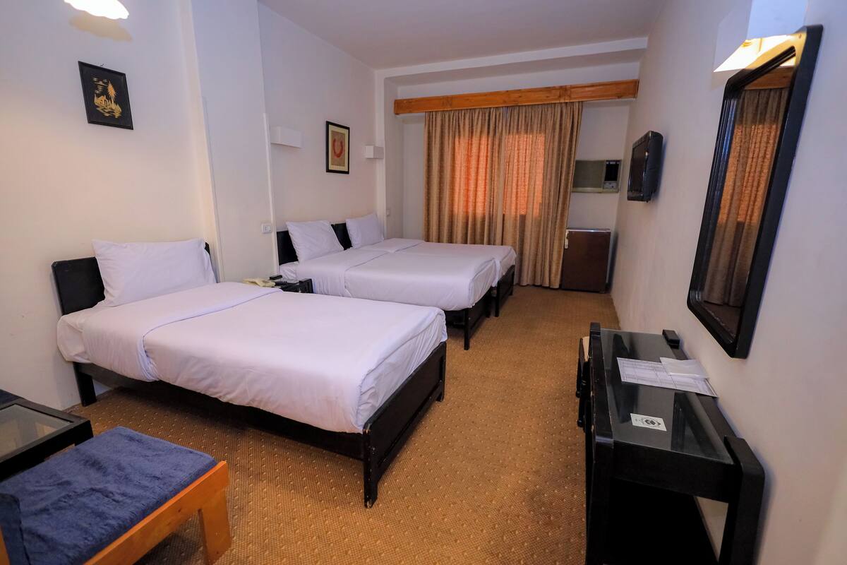 A hotel room with two beds, a desk, a chair, and a mirror.