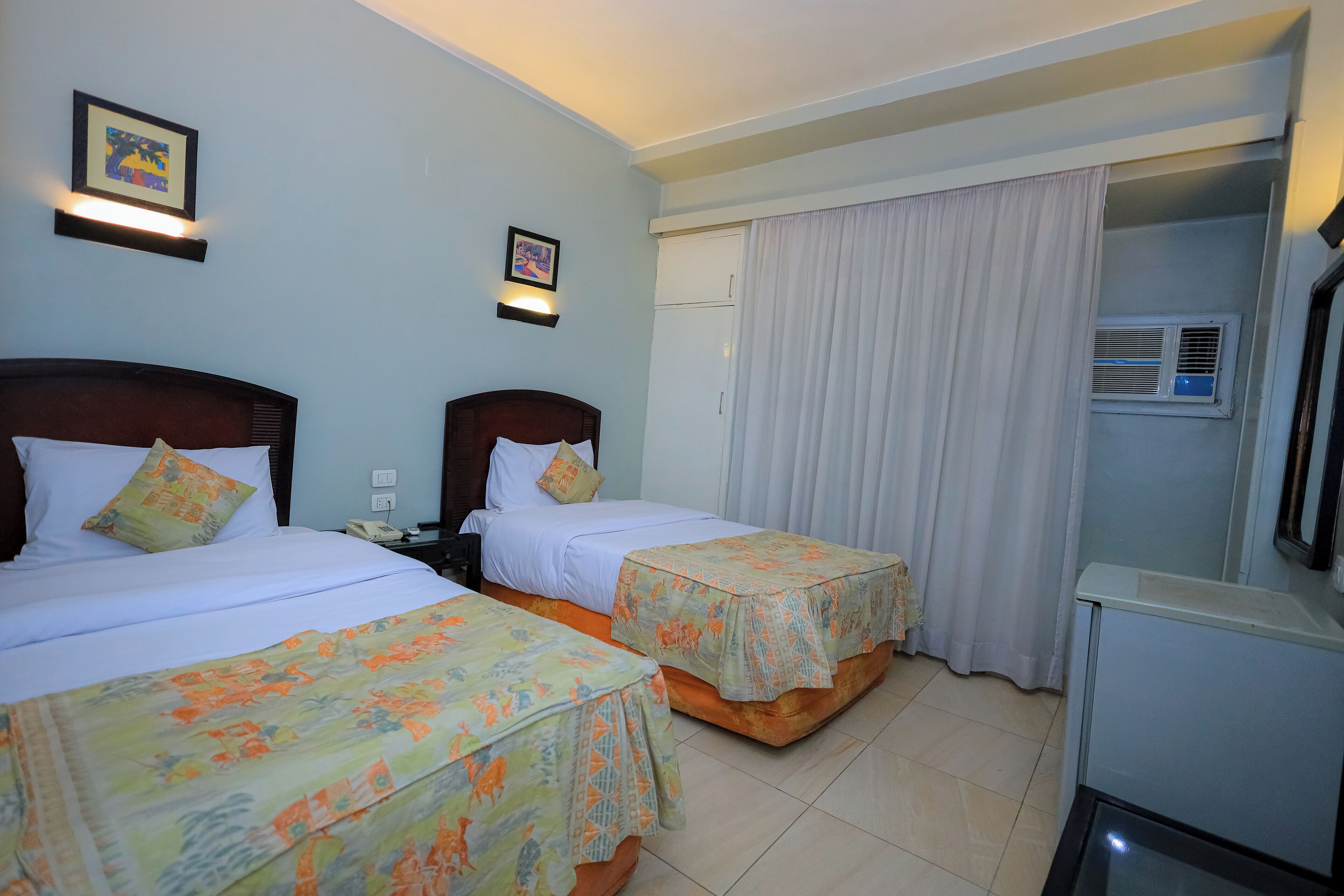 Habitación de hotel con dos camas, un escritorio, una silla, un refrigerador y un equipo de aire acondicionado.