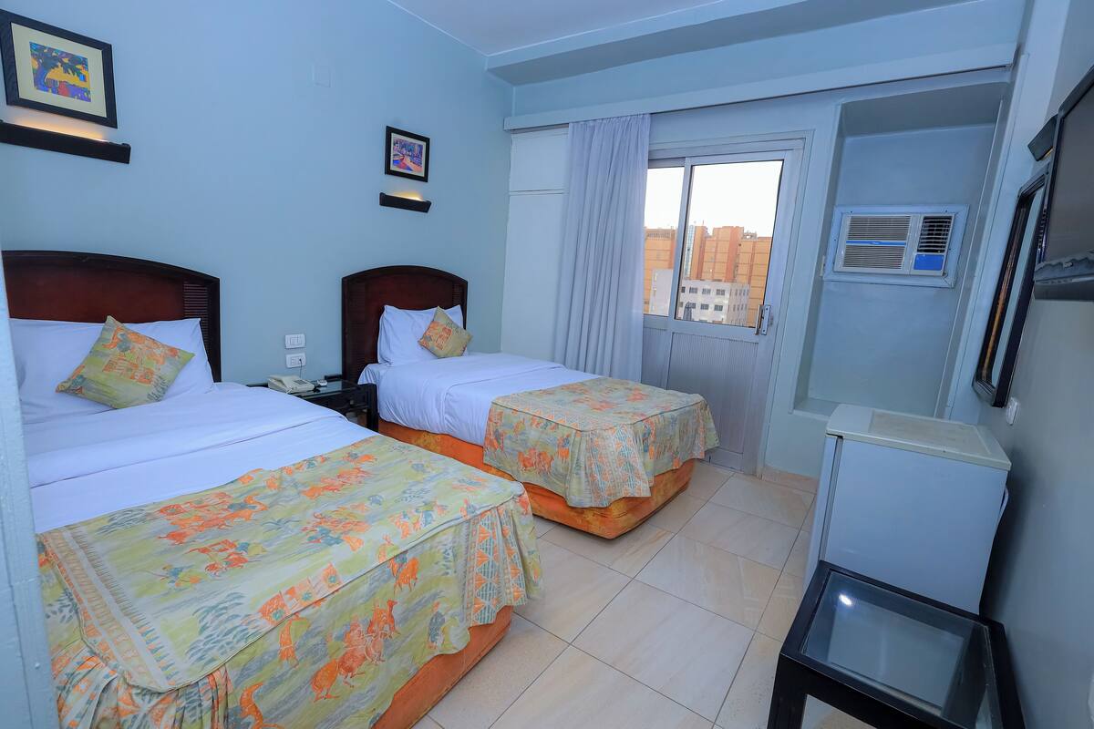 A hotel room with two beds, a small table, and a window with curtains.