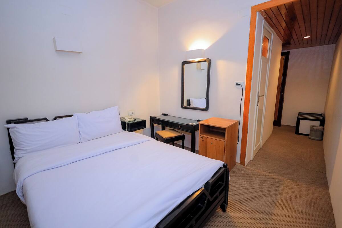 A hotel room with a bed, a desk, a chair, a mirror, and a door leading to another room.