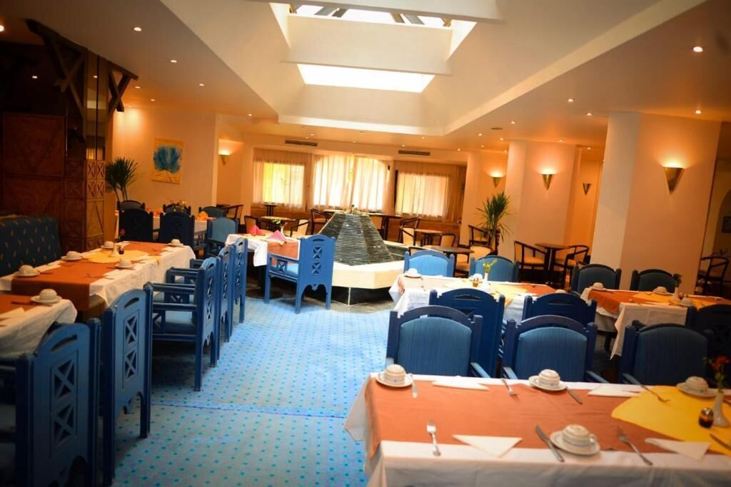 Un comedor de hotel con varias mesas y sillas, un piano en el centro y un suelo estampado.