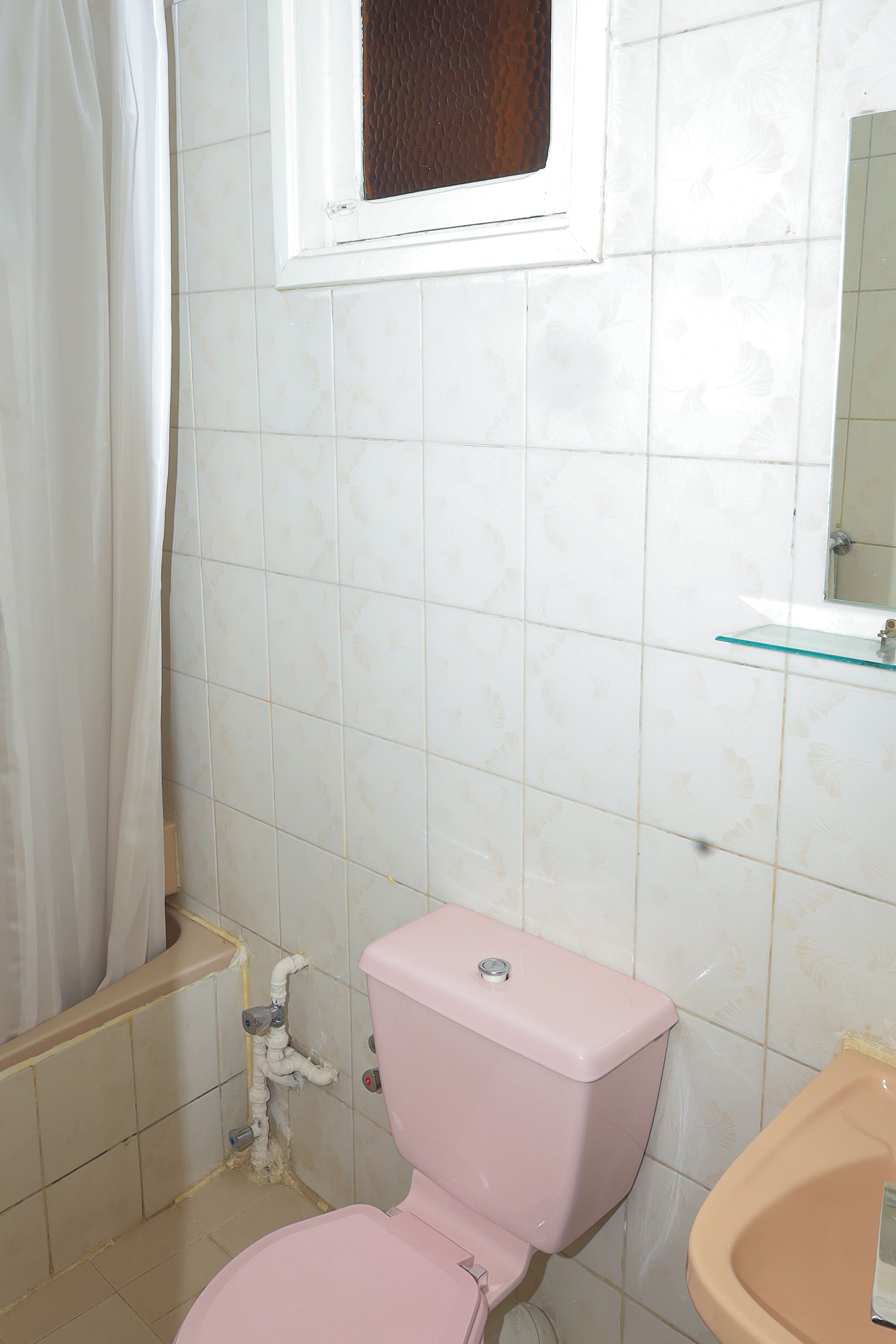 Un baño con un inodoro rosa, un lavabo de cristal y una cortina de ducha.