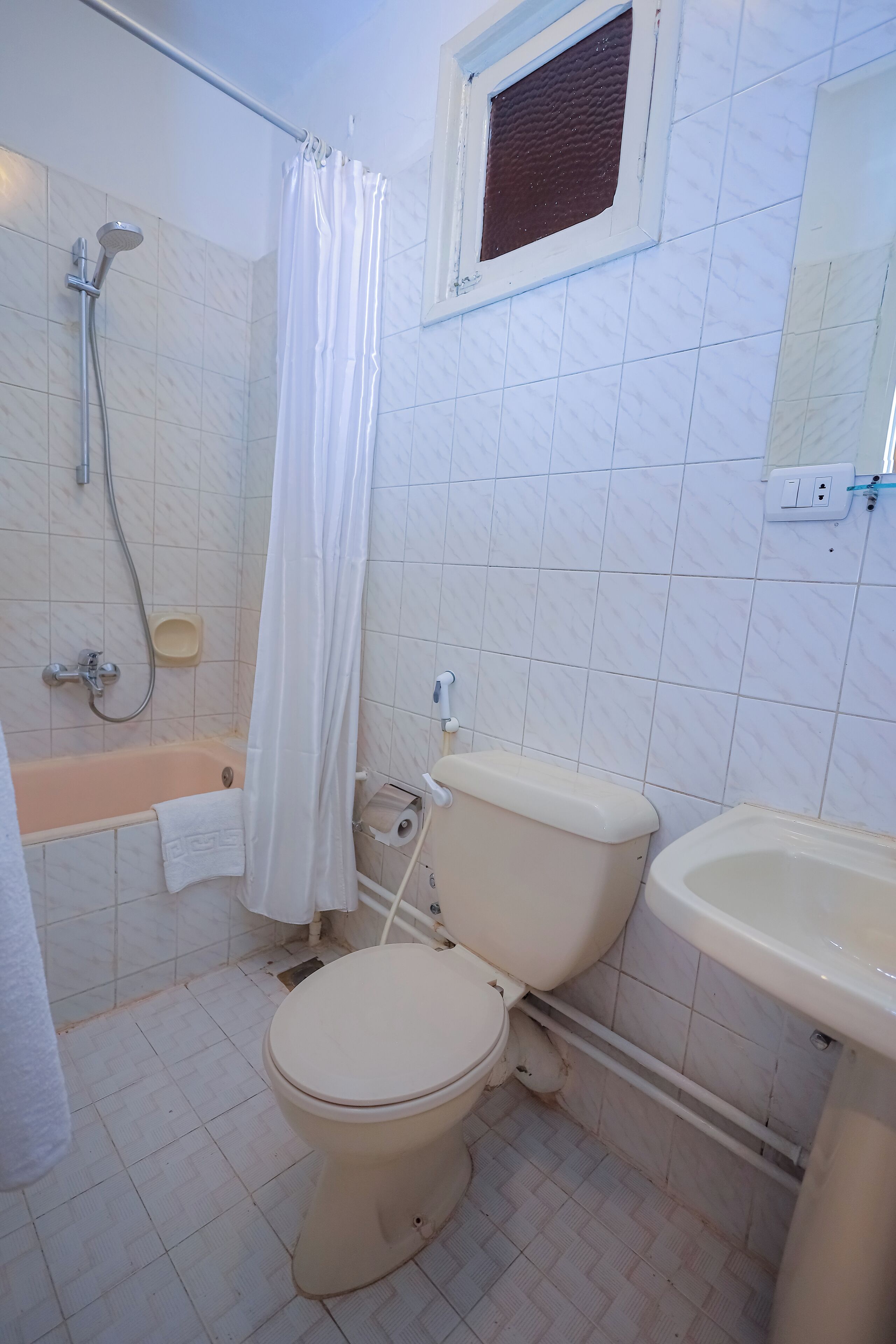 Un baño con inodoro, lavamanos, ducha y una ventana pequeña.