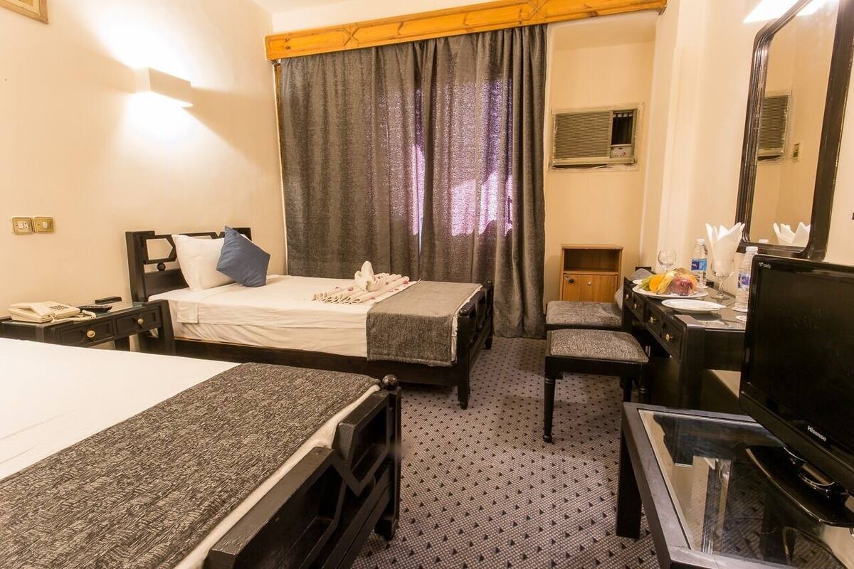 A hotel room with two beds, a desk, a television, and a bathroom with a shower and toilet.