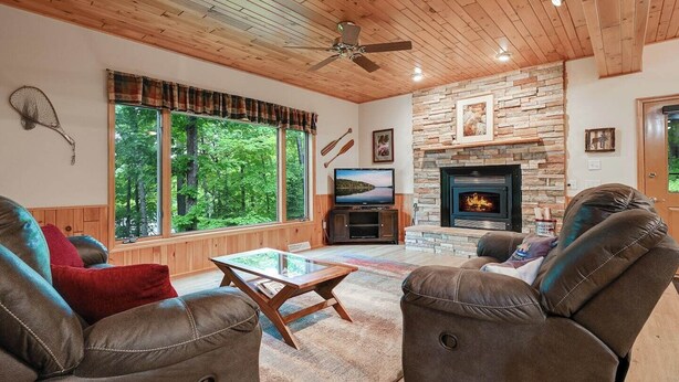 Una sala de estar acogedora con chimenea de piedra, sofás de cuero, una mesa de centro de vidrio y ventanas amplias con vistas al bosque.