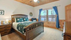 Un dormitorio con una cama de madera, una mesita de noche, un escritorio, una ventana con cortinas y un ventilador de techo.