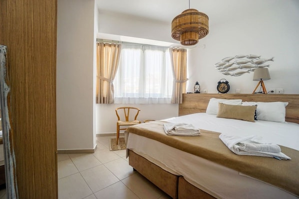 A hotel room with a large bed, a wooden headboard, a window with curtains, a bedside table with a lamp, and a wall clock.