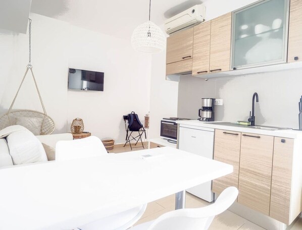 A modern kitchen with white cabinetry, a dining table, and a hanging light fixture. - Urban beach sun(1c) The ultimate urban beach vibe. (Rethymno)